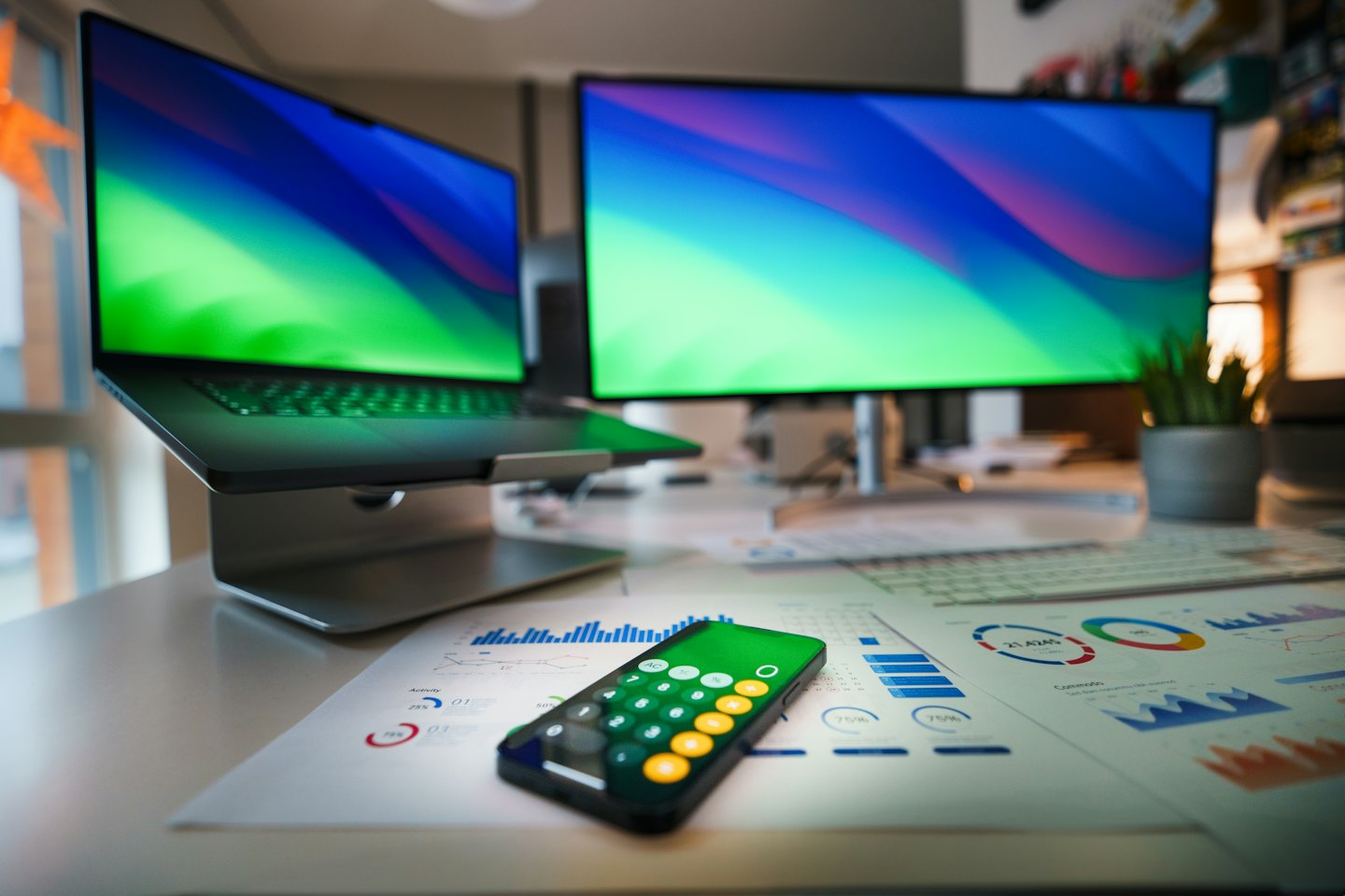 Escritorio con portátil, monitor y papeles con gráficos.